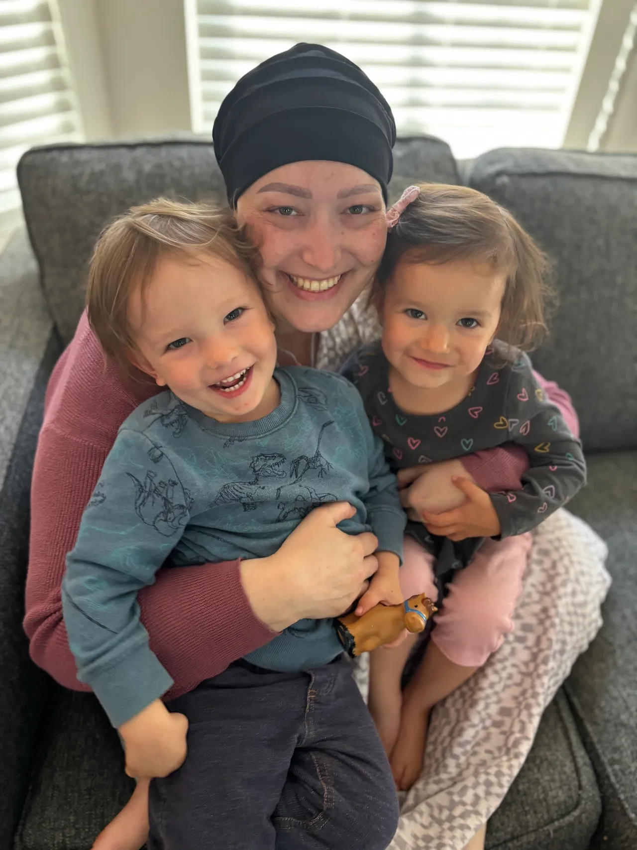 A joyful woman hugging two smiling children on a couch.