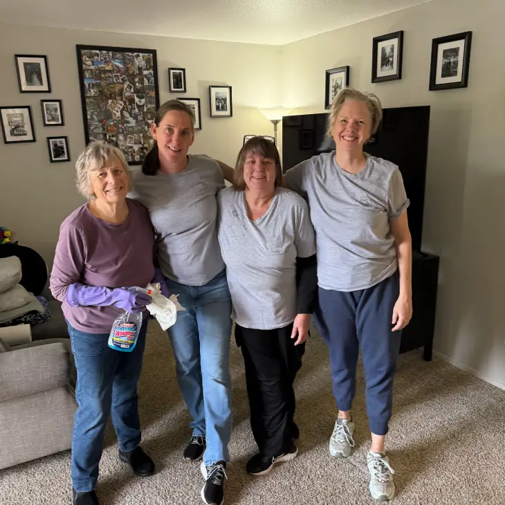 Four women standing together in a cozy living room, smiling.