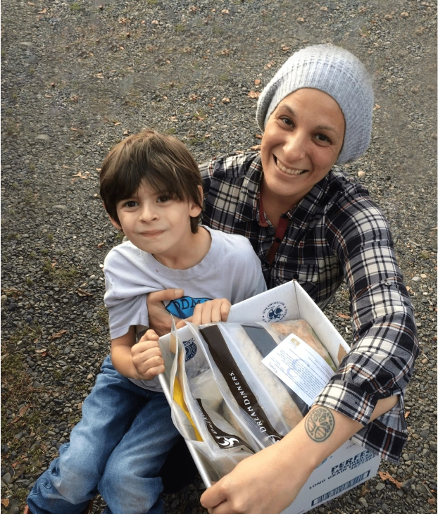 Woman and child smiling outdoors, holding a book.