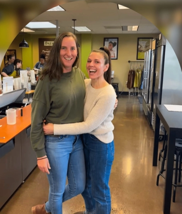 Two women smiling and hugging in a cozy cafe.