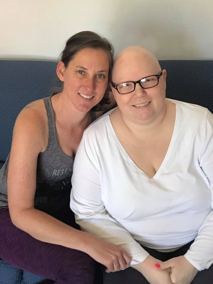 Two women sitting closely together, smiling warmly at the camera.