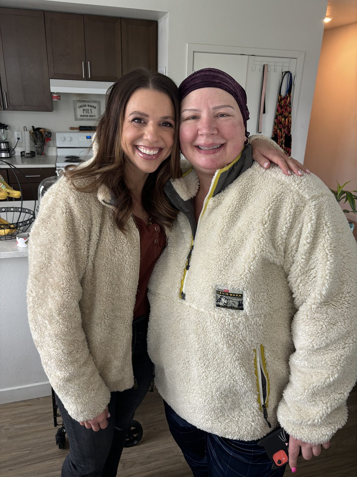 Two smiling women wearing cozy fleece jackets in a kitchen.