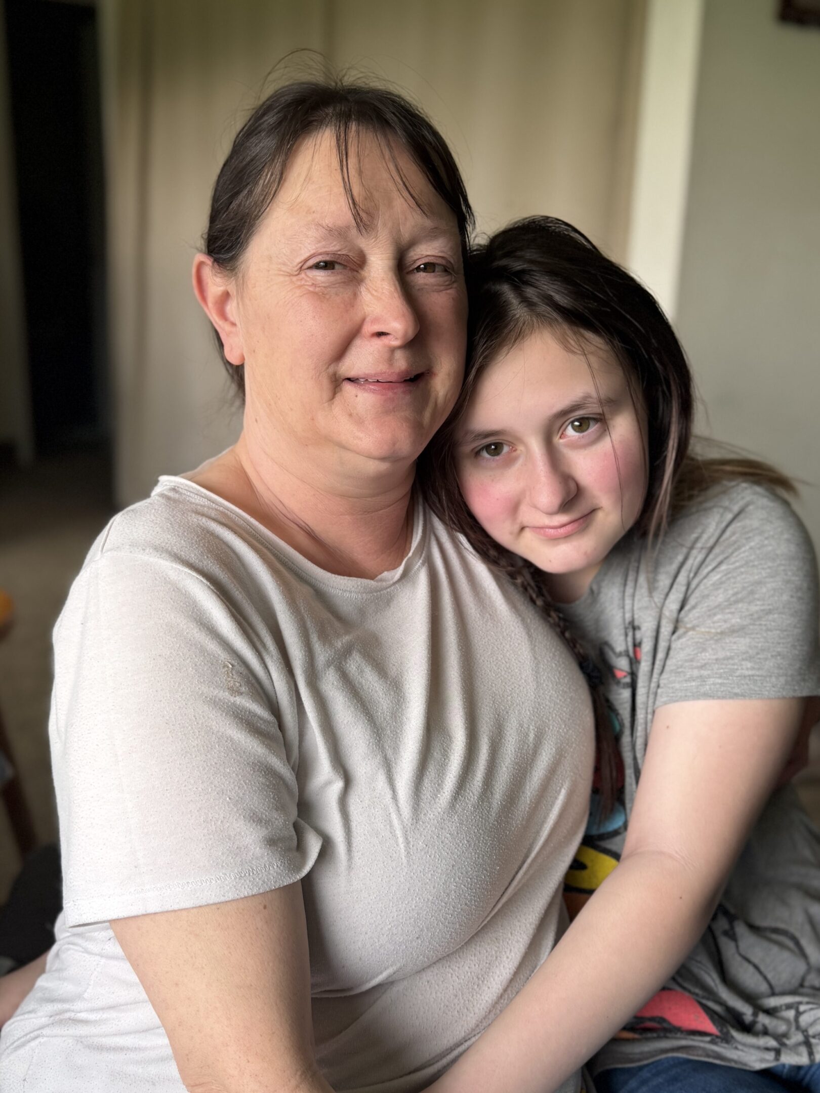 A woman and a young girl share a warm embrace indoors.